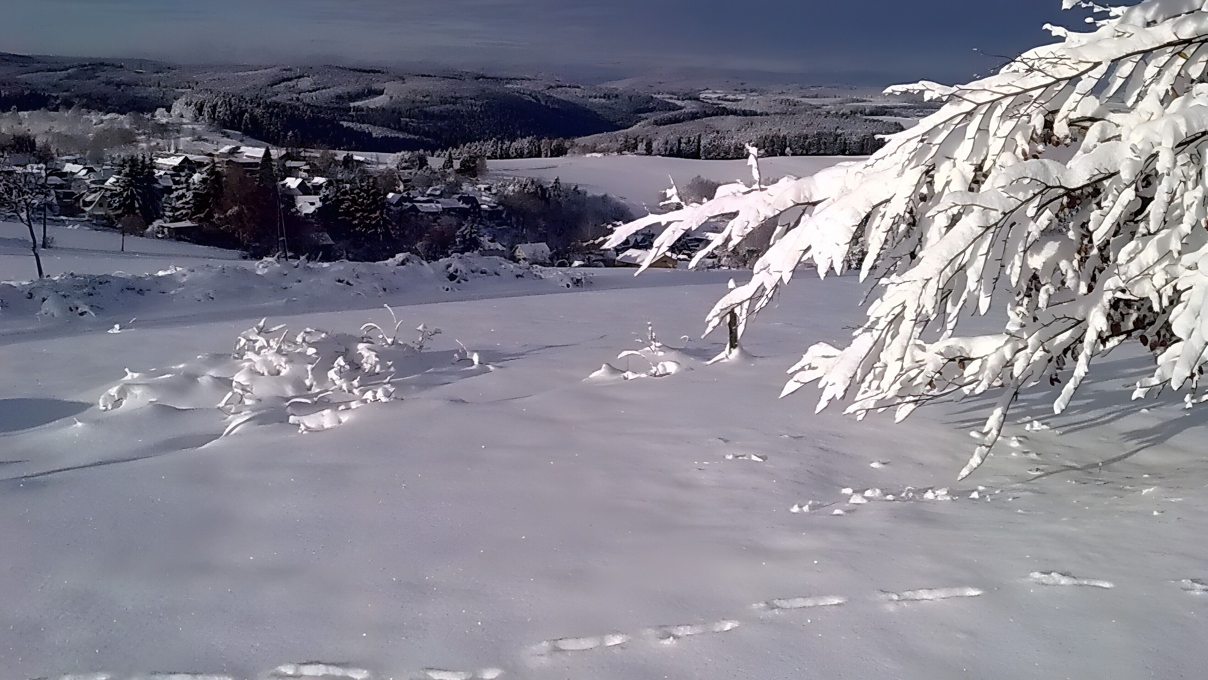 A snowy landscape with a clear view of a valley and distant hills.