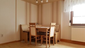 Et spiseområde med et træbord og stole, et vindue med gardiner samt en radiator.