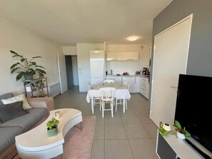 Una sala de estar moderna con un sofá, una mesa de comedor con sillas, un televisor y una cocina al fondo.