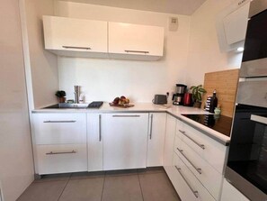 Una cocina moderna con armarios blancos, horno empotrado y una encimera con electrodomésticos y un frutero.