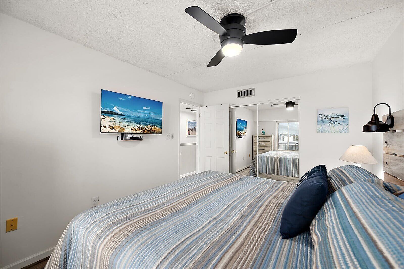 A bedroom with a bed, a ceiling fan, a TV, and artwork on the walls.