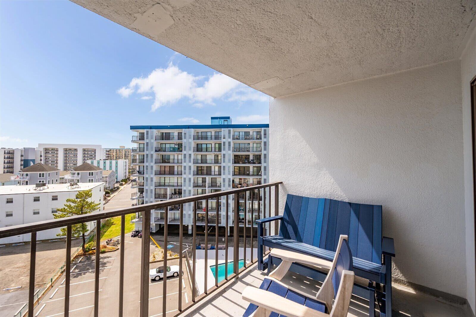 A balcony with a pool, lounge chairs, and a view of a multi-story building.