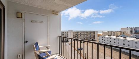 A balcony with a door labeled 'FLAMINGO LOUNGE,' a railing, and a view of a parking lot and buildings.