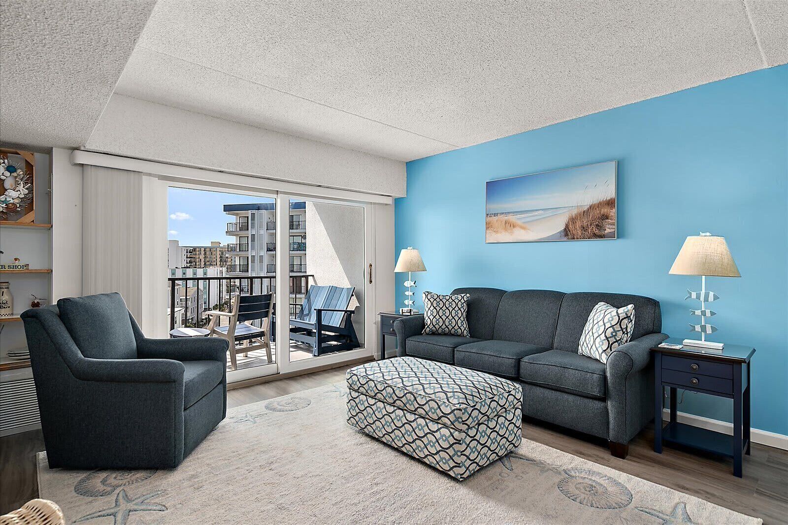 A modern living room with a balcony, a sofa set, a patterned ottoman, and a view of the cityscape.