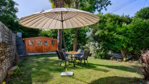 Eine Terrasse mit Tisch, Stühlen, einem Sonnenschirm und einem hölzernen Gartenhaus.