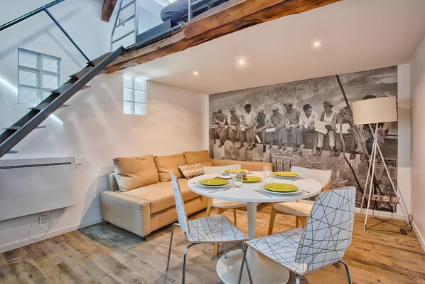 Un salon moderne avec une table à manger pour quatre personnes, un escalier et une grande fresque murale en noir et blanc.