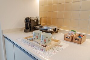 A kitchen area with a coffee maker, two floral mugs, a tray with a spoon, and two wooden boxes with tea bags. - A charming studio apartment in an extremely convenient location, with the subway practically on your doorstep: Turin city center can be reached in about six minutes, while the San Salvario neighborhood is even closer. The apartment is a short distance fr (Turin)