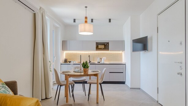 Een moderne keuken met een eethoek, een aan de muur bevestigde televisie en een deur met een greep.