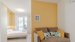 Een kamer met een bed, een bank, een raam met gordijnen en een ingelijste foto aan de muur.