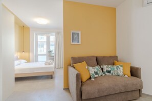Ein Zimmer mit einem Bett, einem Sofa, einem Fenster mit Vorhängen und einem gerahmten Bild an der Wand.