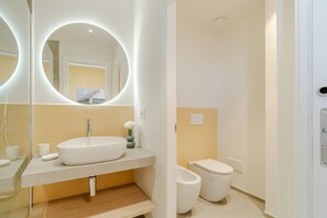 Ein modernes Badezimmer mit einem großen, ovalen Spiegel, einem weißen Waschbecken und einer Toilette.