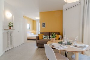 Ein modernes Wohnzimmer mit Essbereich, einer Sofagarnitur, einem Blumentopf und einem gerahmten Bild an der Wand.