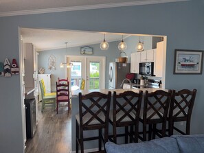 A kitchen with a refrigerator, microwave, and dining area with chairs and a table. - 3bd/2bth home in Keys @ OceansideVillage-3 min walk to the beach! Golfcart avail (Surfside Beach)