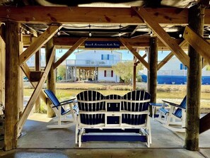 A wooden gazebo with a bench and two chairs, a sign reading 'Beach Memories Here,' and a view of a house and beach in the background. - 3bd/2bth home in Keys @ OceansideVillage-3 min walk to the beach! Golfcart avail (Surfside Beach)