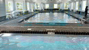 Ein Hallenbad mit klarem Wasser, einer gefliesten Liegefläche und Stühlen entlang der Seiten.