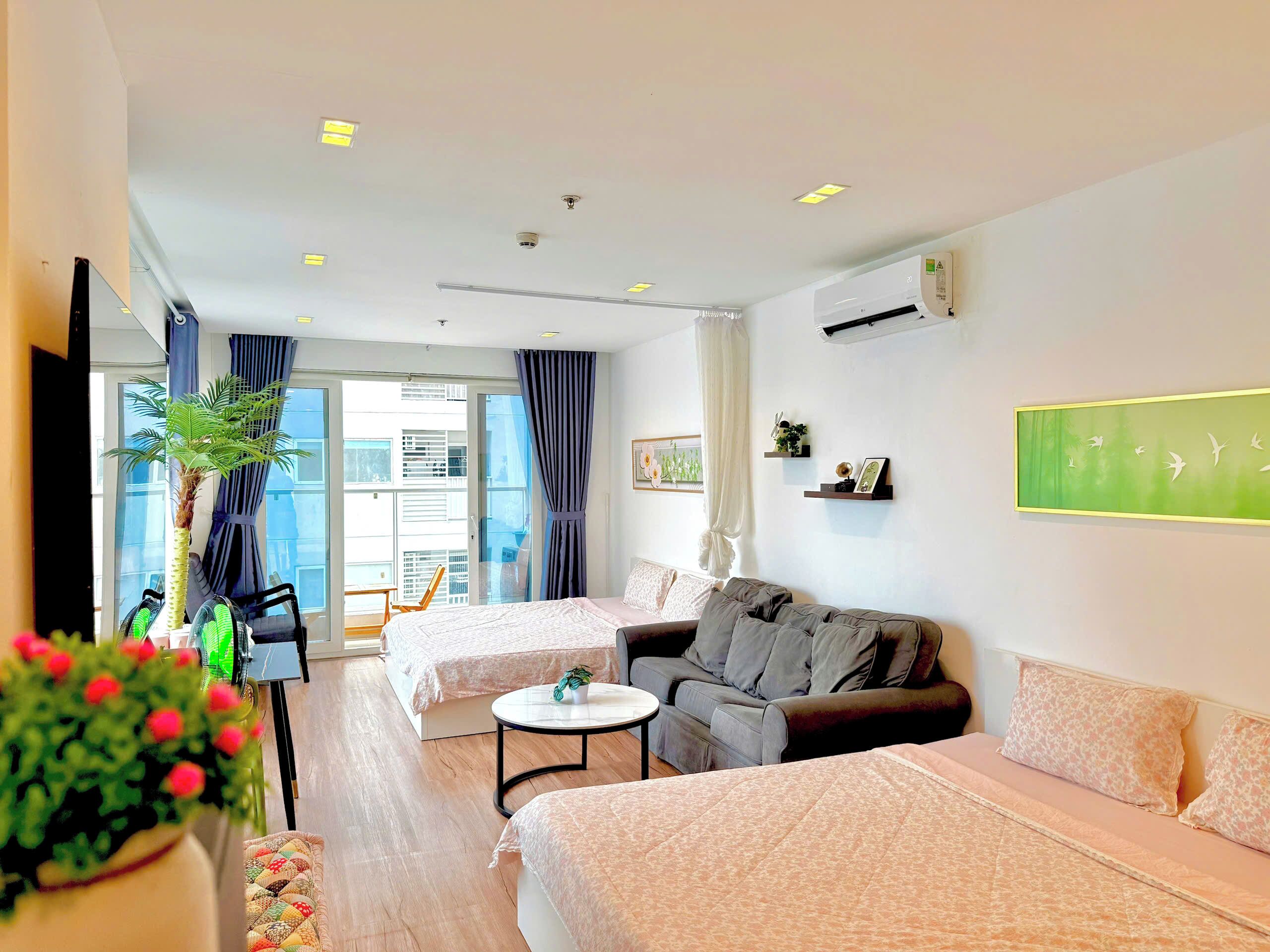 A hotel room with two beds, a sofa, a small table, a TV, and a balcony with curtains.