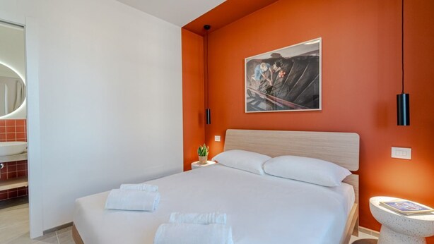 Une chambre d’hôtel avec un grand lit, un tableau au mur, une petite table avec une plante et une salle de bain avec un miroir et un lavabo.