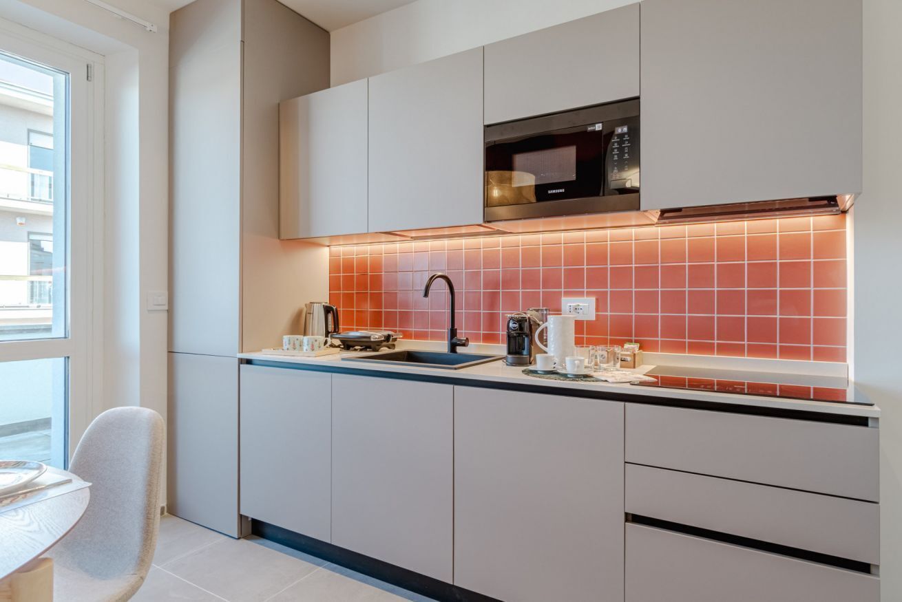 A modern kitchen with white cabinets, a black microwave, and a red-tiled backsplash.