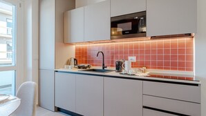 Une cuisine moderne avec des meubles blancs, un micro-ondes noir et un dosseret de cuisine recouvert de carreaux rouges.