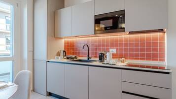 A modern kitchen with white cabinets, a black microwave, and a red-tiled backsplash.