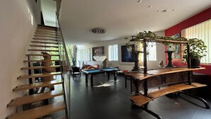 Uma sala de estar ampla com mesa de bilhar, um banco de madeira e uma escada.