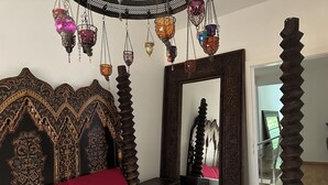 Quarto com cama grande, cabeceira decorativa, espelho e lanternas penduradas.