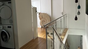 Uma cozinha moderna com máquina de lavar, escada em espiral e uma concha decorativa na parede.