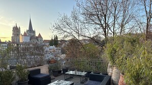 Terraço no telhado com mobiliário de exterior, plantas em vasos e vista para edifícios históricos.