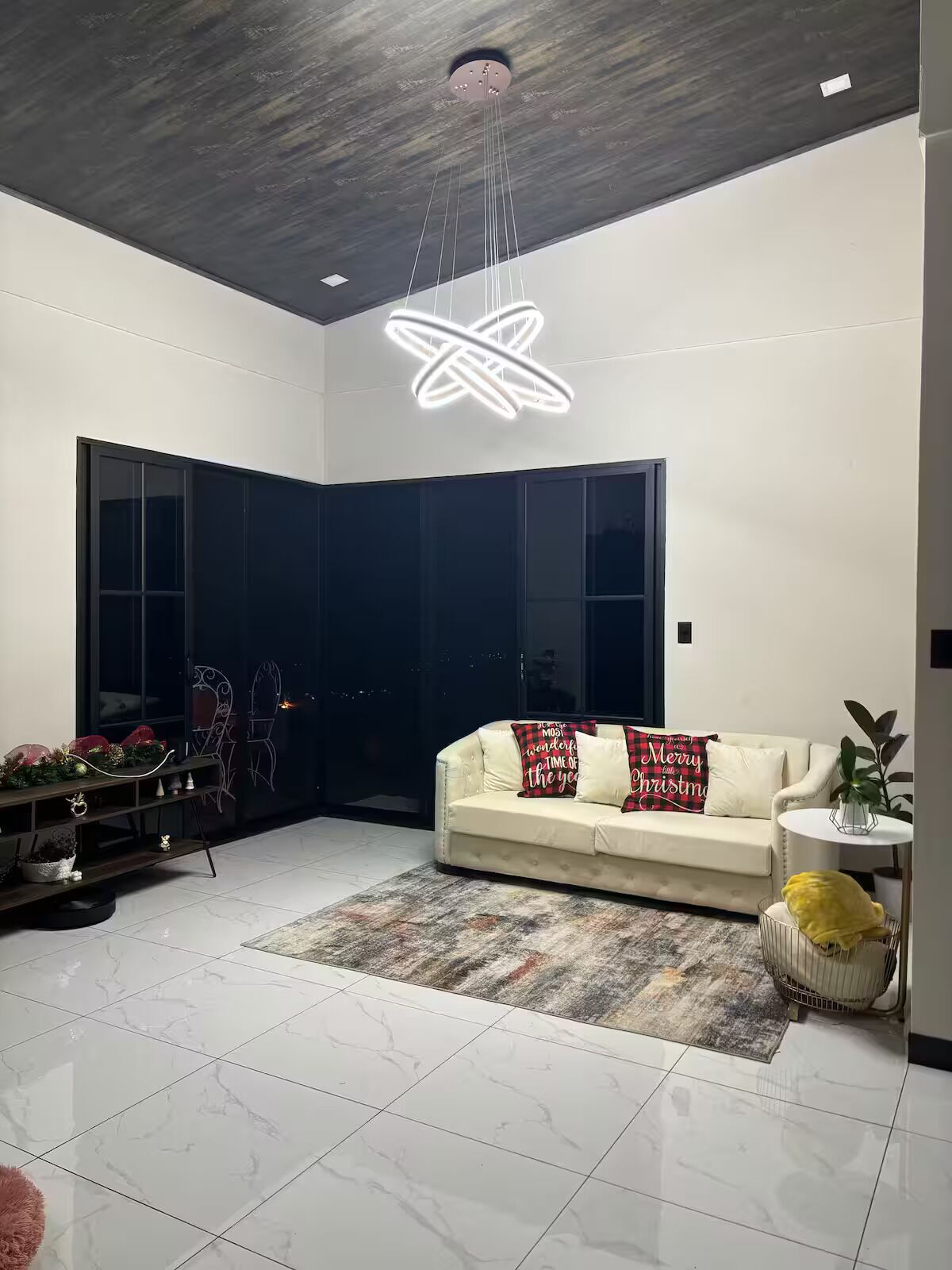A modern living room with a sofa, a decorative ceiling light, a large window, and a plant.