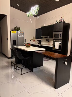 Una cocina moderna con una isla central, taburetes de bar, horno empotrado y microondas.