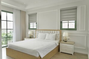 Un dormitorio con una cama grande, dos mesitas de noche con lámparas y vistas al verdor por una ventana.