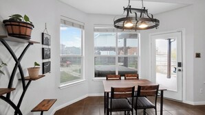 A dining area with a table and chairs, a hanging light fixture, and potted plants on shelves. - Spacious 4BR Retreat |Pool Table| Firepit & Hottub (Kyle)