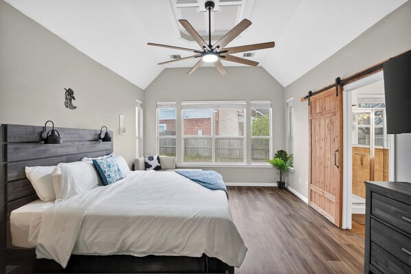 A bedroom with a bed, a ceiling fan, a large window, and a sliding door.
