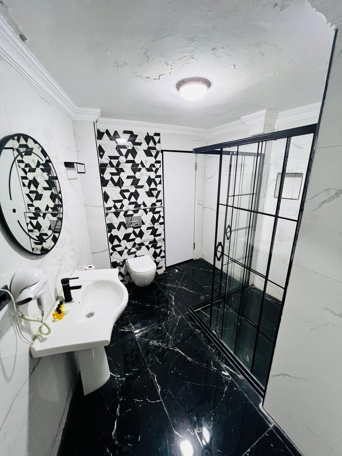 Ein Badezimmer mit weißem Waschbecken, Spiegel, Toilette und schwarzem Marmorboden.
