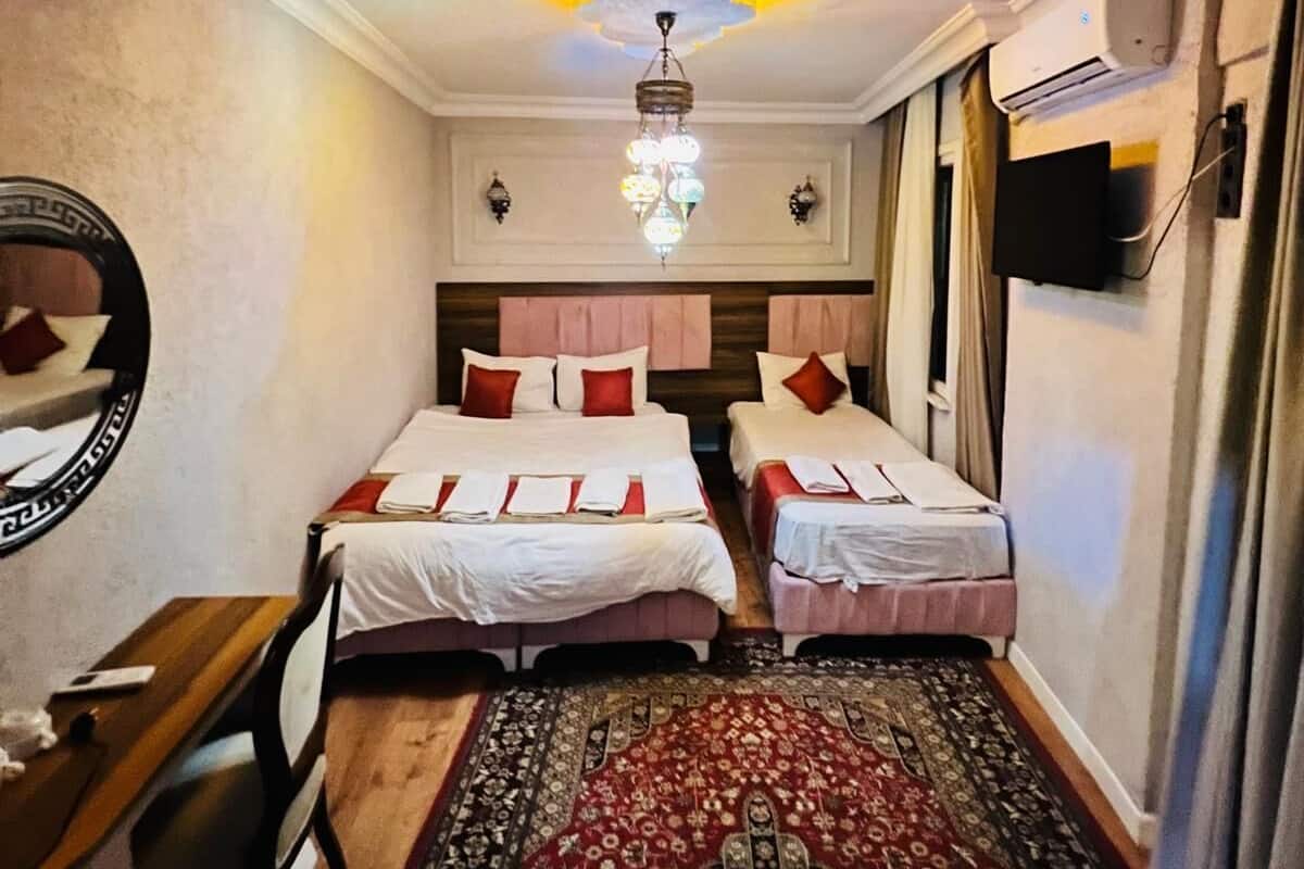 Une chambre d’hôtel avec deux lits, un bureau, une chaise, un lustre, un appareil de climatisation et un tapis à motifs.