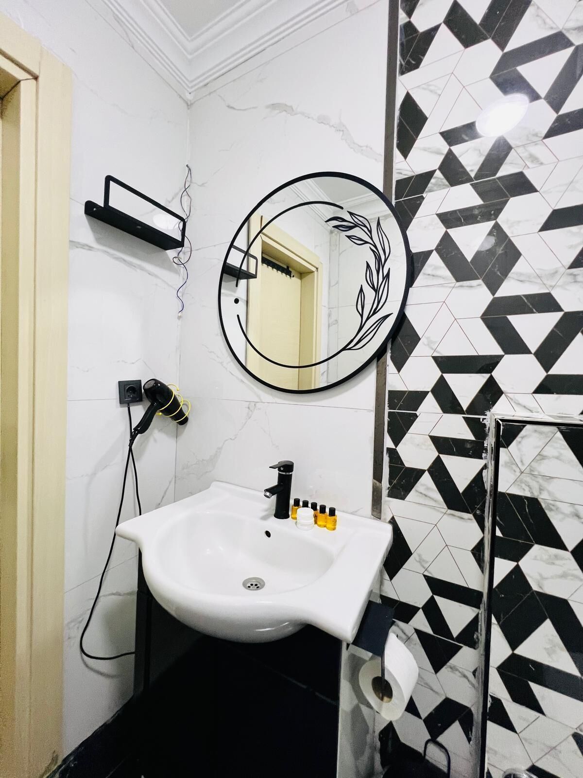 A bathroom with a white sink, black and white patterned tiles, a mirror with a decorative frame, and a towel rack.
