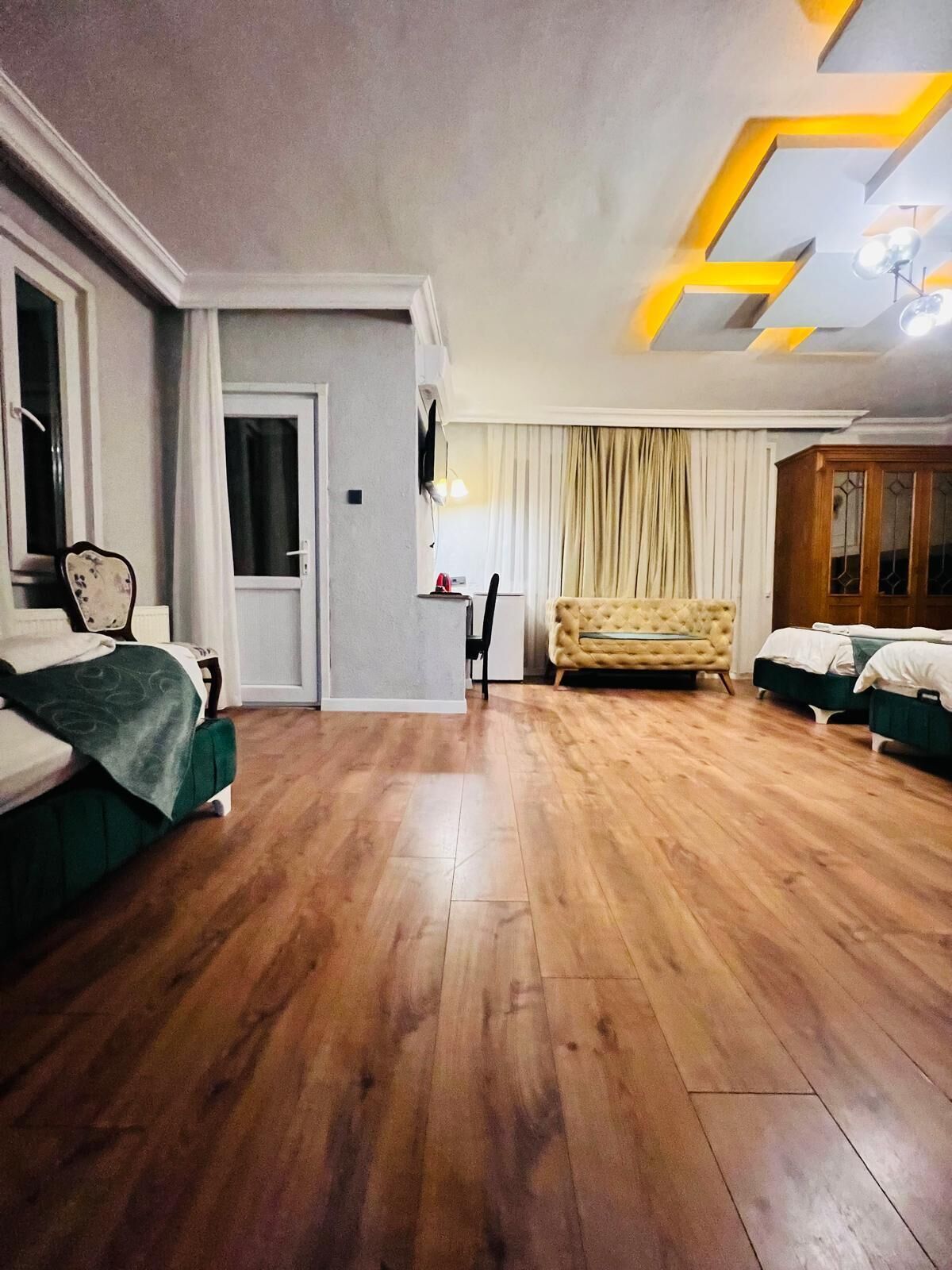 Una habitación de hotel con suelo de madera, un sofá, una cama, un televisor y una ventana con cortinas.