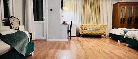 Una habitación de hotel con suelo de madera, un sofá, una cama, un televisor y una ventana con cortinas.