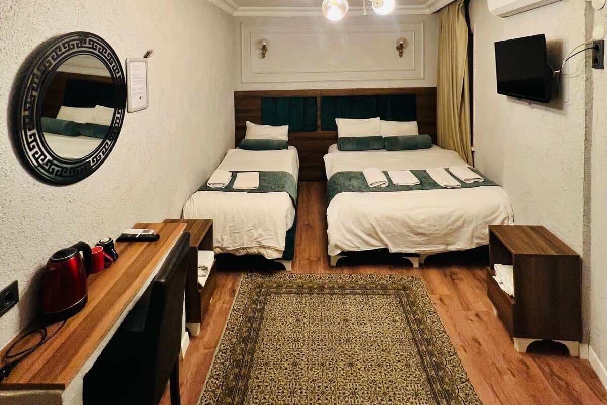 Une chambre d’hôtel avec deux lits, un bureau, un miroir, une télévision et un luminaire au plafond.
