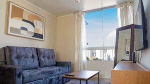 Una sala de estar con sofá, mesa de centro, televisor y balcón con cortinas.