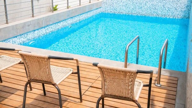 Una piscina con borde de azulejos, cubierta de madera y dos sillones de mimbre.