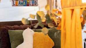 A plush toy on a bed with a patterned rug, a hanging sign, and a lamp.