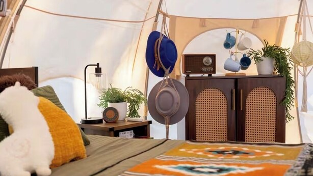 A cozy tent interior with a bed, a radio, and a cabinet with hanging items.