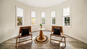 A room with four windows, a round wooden table, two wooden chairs, and a woven rug. - NEW! Boho Bungalow (Carolina Beach)