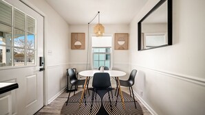 A hallway with a white door, a round table with four chairs, a hanging light fixture, and two wall-mounted picture frames. - NEW! Boho Bungalow (Carolina Beach)