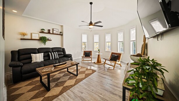 A living room with a black sofa, a coffee table, a ceiling fan, and a wooden floor. - NEW! Boho Bungalow (Carolina Beach)