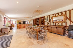 Ein geräumiger Essbereich mit einem langen Holztisch und Korbstühlen, eine Küche mit Backsteinwand und Holzbalken sowie eine Treppe, die zu einer oberen Ebene führt.