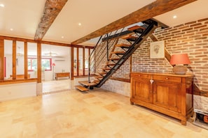 A spacious room with a wooden staircase, a brick wall, and a wooden cabinet with a lamp. - Terre Adélie •  6 bedrooms | Sauna | 6 min Honfleur (Équemauville)