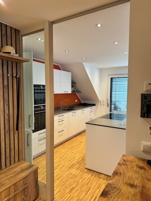 A modern kitchen with white cabinets, a built-in oven, and a wooden floor. - Relaxing vacation apartment at our country estate on the Lower Rhine "Apartment Tenbrockskate" (Hamminkeln)