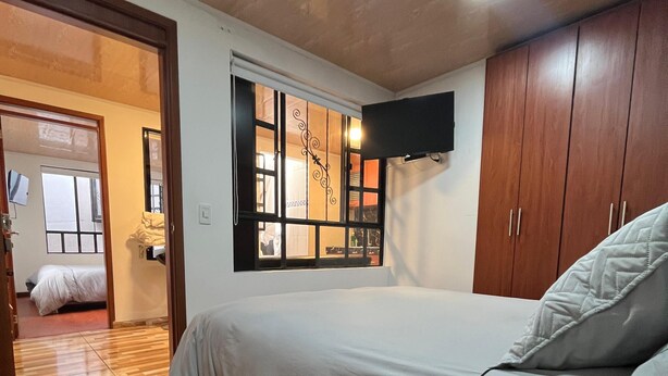 Une chambre à coucher comprenant un lit, un plancher en bois, une fenêtre avec des rideaux, une armoire et un téléviseur à écran plat fixé au mur.